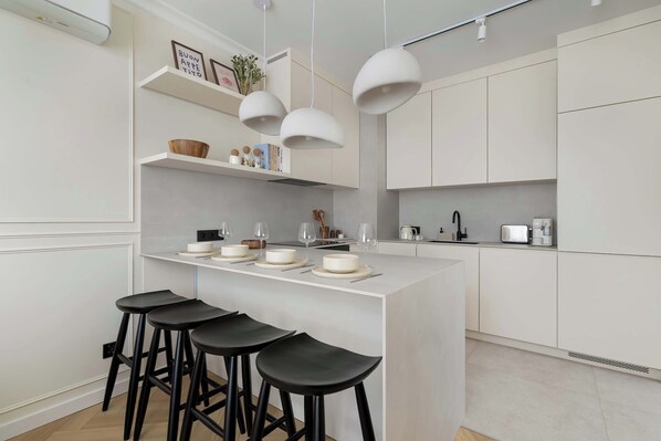 A modern kitchen with a central island, bar stools, pendant lights, and white cabinetry.