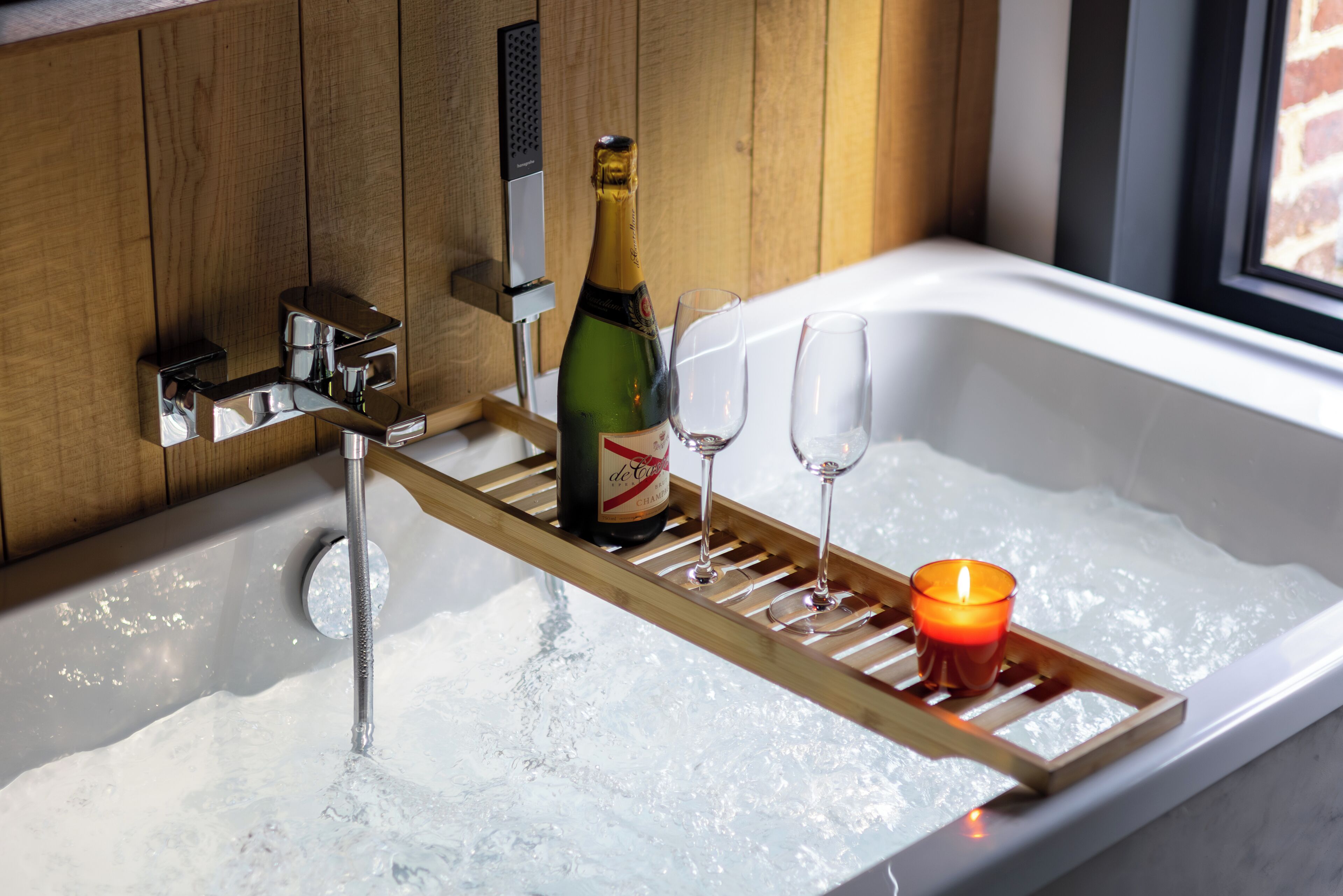 Eine Badewanne mit einer Champagnerflasche, zwei Gläsern und einer Kerze auf einem Tablett.