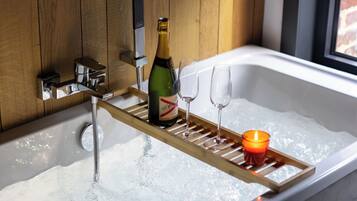 Eine Badewanne mit einer Champagnerflasche, zwei Gläsern und einer Kerze auf einem Tablett.