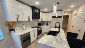 Una cocina moderna con armarios blancos, una isla de mármol, una silla negra y un colgante de luz.