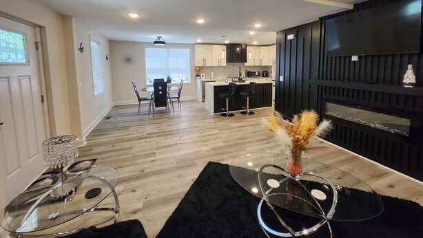 Una cocina moderna con armarios oscuros, un mueble de TV negro y una zona de comedor con una mesa y sillas de vidrio.
