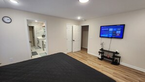 Un dormitorio con una cama, un televisor montado en la pared y una puerta que da al baño.