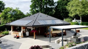 Un petit bâtiment d’un seul étage, doté d’un toit en pente, d’un espace extérieur abrité avec des sièges et d’un petit jardin agrémenté de plantes en pot.