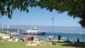 Un parc au bord de l’eau où l’on peut voir des gens se détendre sur l’herbe, un bateau amarré au quai et une vue dégagée sur l’eau.