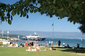 Un parc amb vistes al mar, persones relaxant-se sobre l'herba, un vaixell amarrat al moll i una vista clara de l'aigua.