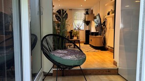 Uma sala de estar moderna com piso de madeira, uma poltrona acolchoada verde e uma área de jantar com mesa e cadeiras.