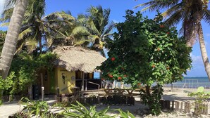Eine Strandhütte mit einem Reetdach, umgeben von Palmen und tropischer Vegetation.