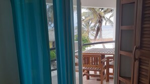Ein Zimmer mit einem Bett, einer Glastür zum Außenbereich mit einem Holztisch und Stühlen sowie Blick auf Palmen und das Meer.