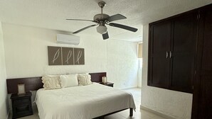 Een slaapkamer met een bed, een plafondventilator, een kledingkast en een wandairconditioner.