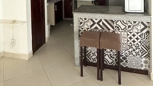 Een kleine keuken met donkerhouten kastjes, een decoratieve spatwand, een witte koelkast en een blauwgroene hanglamp.