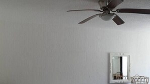 A room with two beds, a ceiling fan, a small table with a basket, and a mirror on the wall.