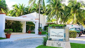 A hotel entrance with a covered walkway, palm trees, and a sign for 'Las Gaviotas Apartment'.