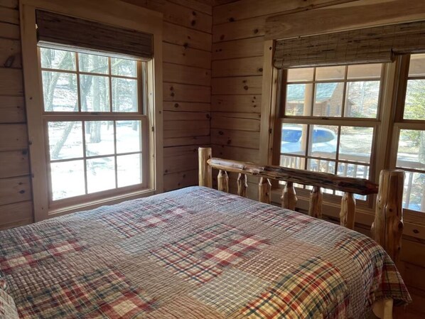 Un dormitorio de cabaña de madera con colcha escocesa, ventanas amplias y un banco de madera.