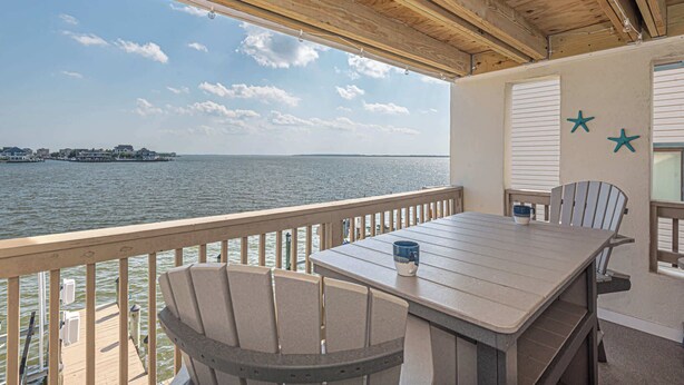 Een houten terras met een tafel en stoelen met uitzicht op een waterpartij.