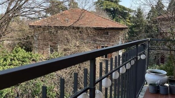 Un balcon avec une balustrade, des plantes en pot et une vue sur une maison dont le toit est recouvert de tuiles.