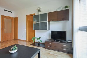 Un salon moderne avec un téléviseur à écran plat, des meubles en bois foncé, une plante en pot et une table basse noire.