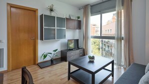 A modern living room with a wooden door, a TV on a cabinet, a dining table, and a sofa. - 5IND1114 - 1 bedroom apartment (Barcelona)