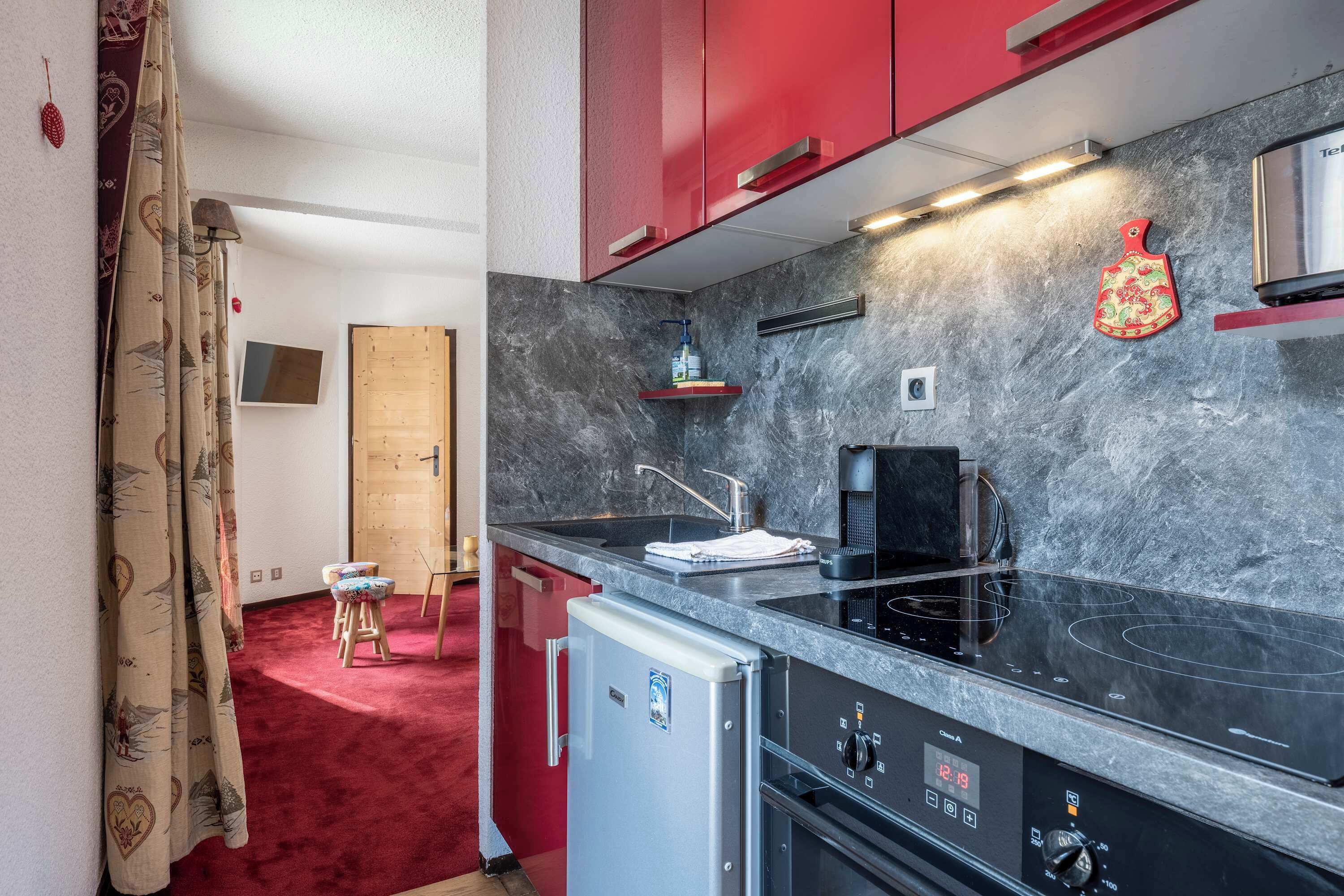 A compact kitchen with a black stovetop, a small refrigerator, and red cabinets.