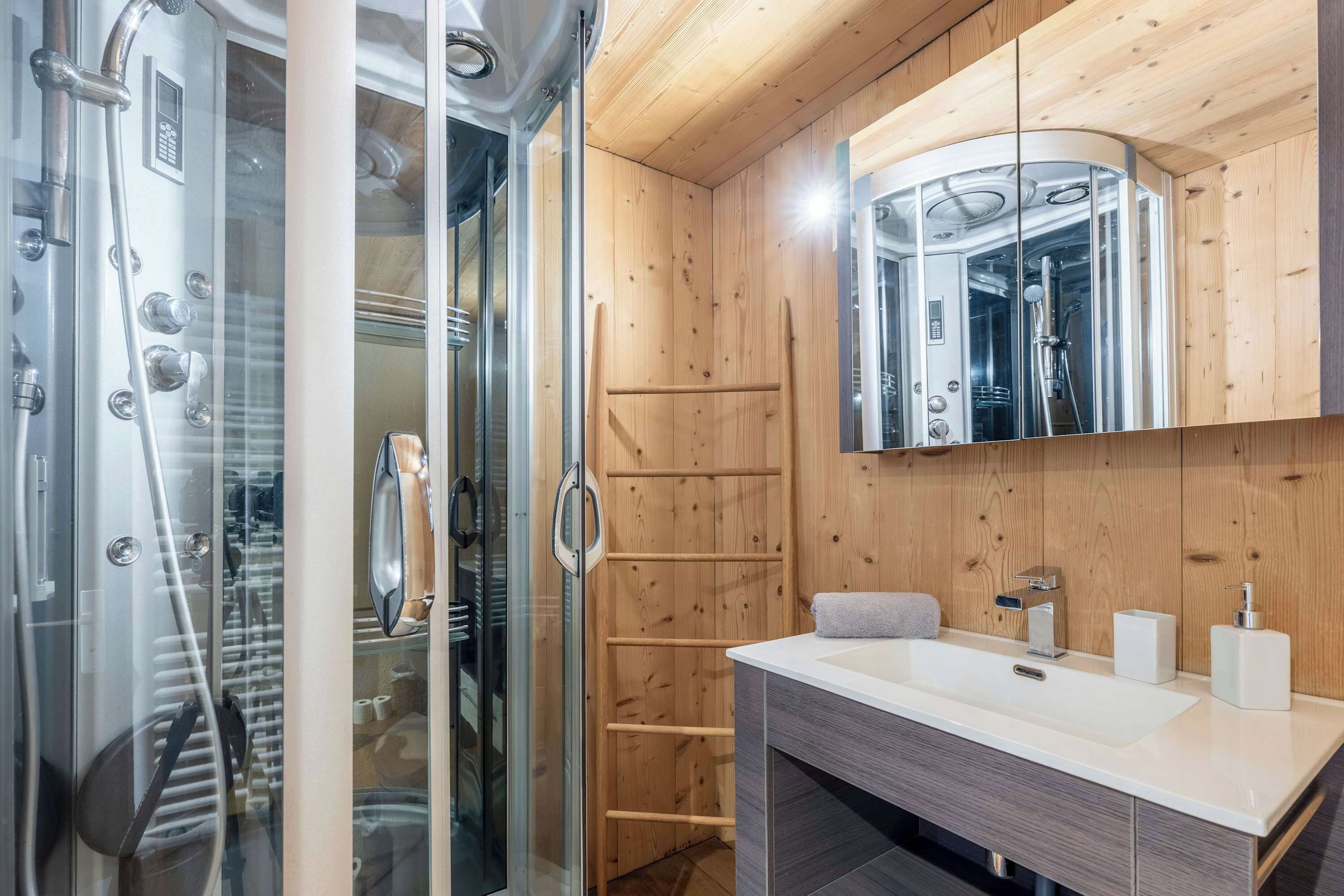 Une salle de bain moderne avec une douche à parois de verre, un lambris en bois, un lavabo blanc et un miroir au-dessus du meuble-lavabo.