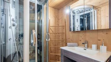 Une salle de bain moderne avec une douche à parois de verre, un lambris en bois, un lavabo blanc et un miroir au-dessus du meuble-lavabo.