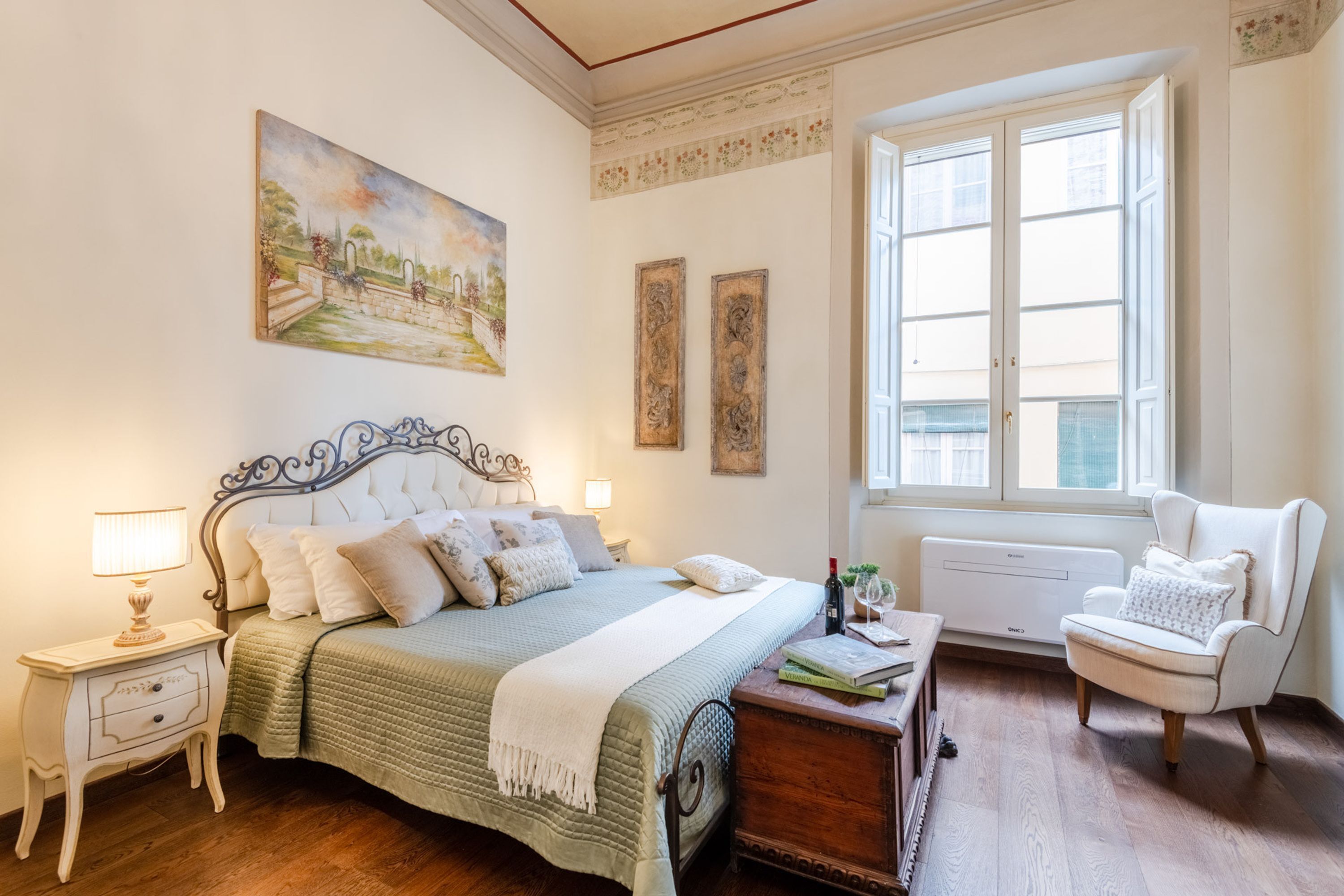 Une chambre à coucher avec un lit, des tables de chevet, une chaise, une fenêtre et un tableau au mur.