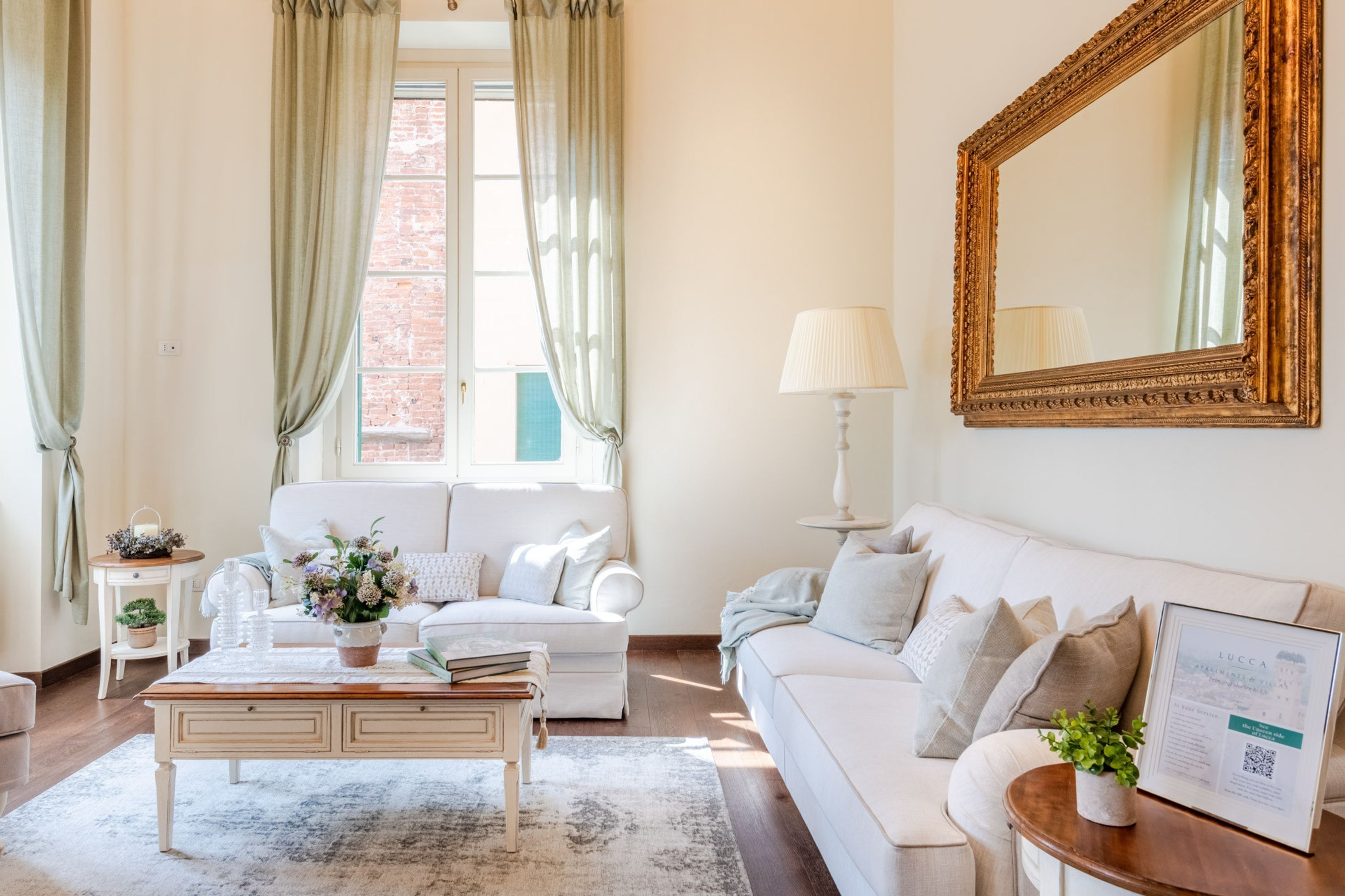 A well-lit living room with a white sofa, a coffee table, and a large mirror on the wall.