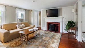 A living room with a beige sofa, a coffee table, a fireplace, and a television on a mantel. - Great Space to be Together and Spread out (Hamilton)