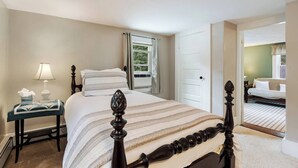 A hotel room with a large bed, a bedside table with a lamp, a window with curtains, and a view of another room. - Great Space to be Together and Spread out (Hamilton)