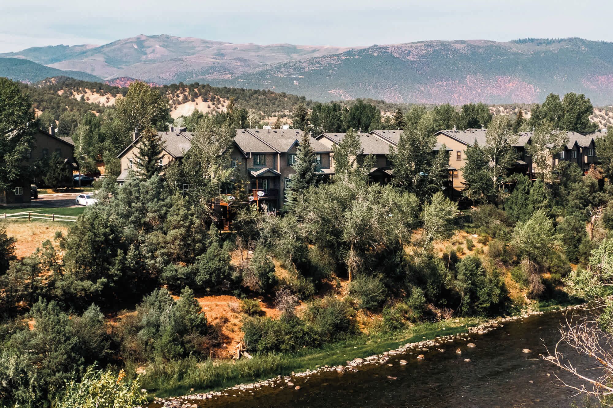 A residential area with multiple houses, a river, and mountains in the background.