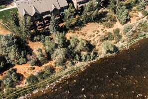 Vista aérea de un albergue con varias construcciones, rodeado de un bosque denso y un río.