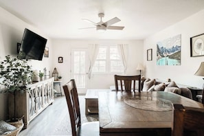 Un comedor con una mesa de madera, sillas, un televisor y un ventilador de techo.