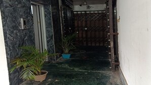 Une entrée fermée par un portail en métal, agrémentée d’un pot de fleurs et d’un chemin en béton menant à un bâtiment.