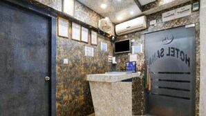 Un comptoir d’accueil avec un revêtement en marbre, des tableaux encadrés accrochés au mur et une porte fermée portant l’inscription « HÔTEL SAIYA ».