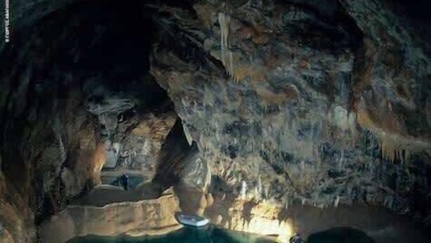 A cave with a turquoise pool, stalactites, and a person kayaking.
