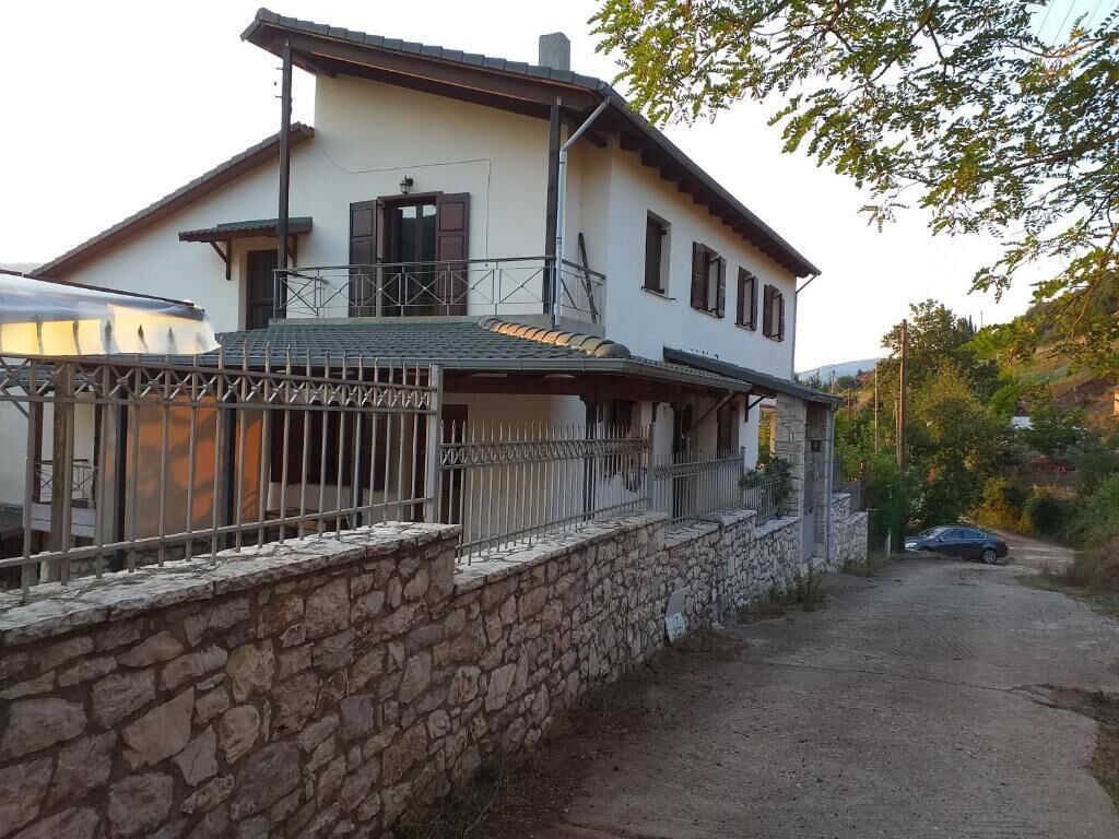 Una casa de dos pisos con un muro de piedra y una cerca de metal al frente.