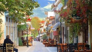 A street lined with shops and cafes, with outdoor seating and a person sitting on a chair.