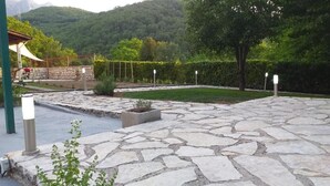 A stone-paved patio with a view of a lush garden and a mountain in the background.