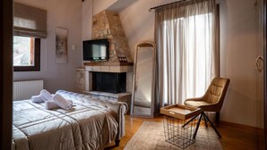 A bedroom with a stone fireplace, a bed with a quilted duvet, a television, and a chair.