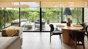 Ein modernes Wohnzimmer mit Deckenventilator, großen Fenstern und Blick auf Grünflächen.