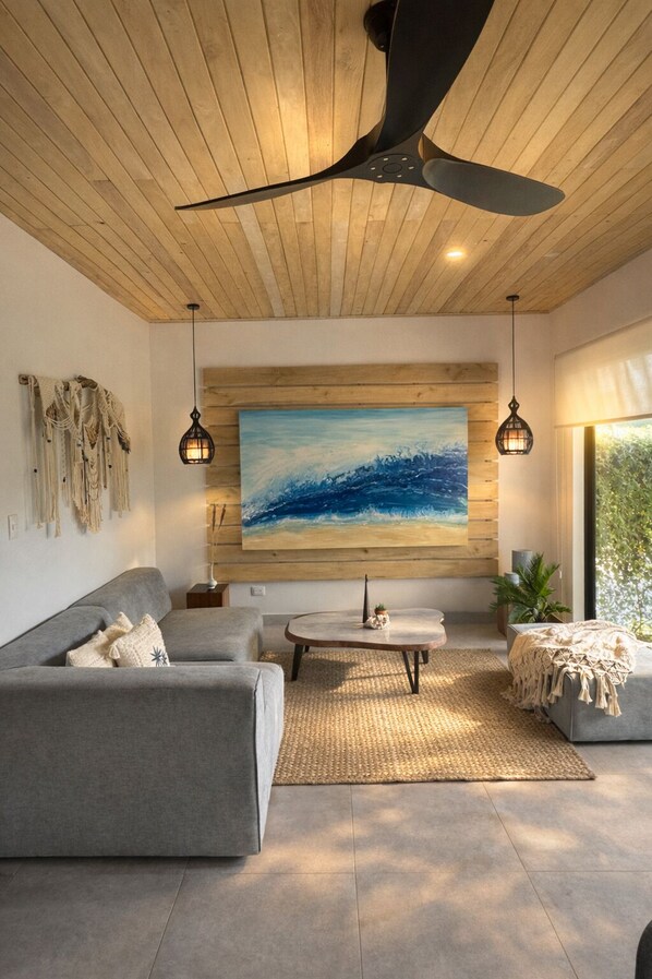 A modern living room with a ceiling fan, a large abstract painting, a grey sofa, a coffee table, and a small plant.