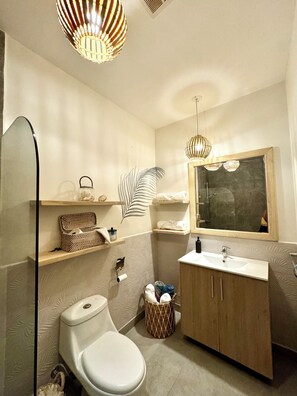 Ein modernes Badezimmer mit Toilette, Waschbecken und Dusche. Es gibt Regale mit Handtüchern und Pflegeprodukten, sowie einen dekorativen Spiegel.