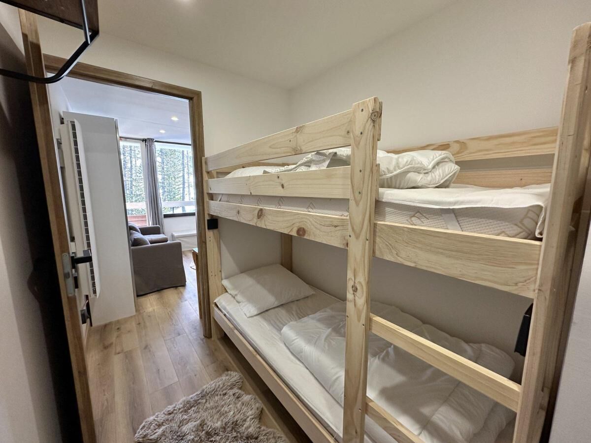 Ein Schlafzimmer mit Etagenbett aus Holz, ein Sofa im angrenzenden Wohnbereich und eine Tür zu einem weiteren Zimmer.