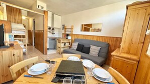 A compact living space with a dining table set for four, a sofa, a kitchenette, and a wooden cabinet.