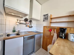 A compact kitchen with white cabinets, a dishwasher, a coffee maker, and a toaster.