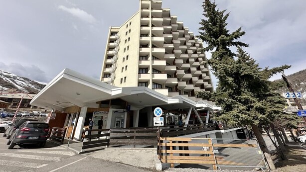 A multi-story hotel with a distinctive architectural design, featuring a central atrium and a parking area in front.
