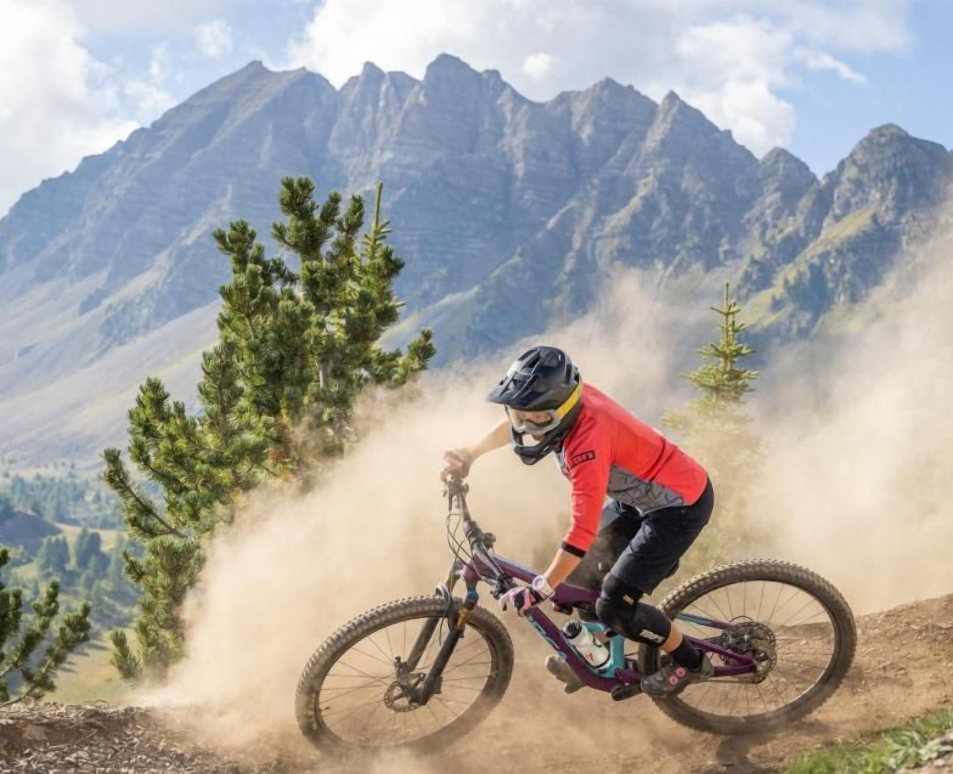 Un ciclista da mountain bike su un sentiero, con montagne sullo sfondo.