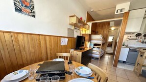 A dining area with a wooden table set for four, a grill, and a kitchen in the background.