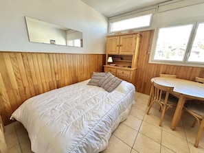 A bedroom with a bed, wooden paneling, a desk, and a chair.