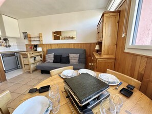 Ein kompakter Wohnbereich mit Esstisch für vier Personen, einer Couch, einer Küchenzeile inklusive Geschirrspüler und Holzschränken.