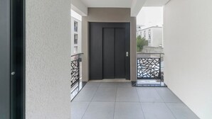 A narrow corridor with a closed door at the end, tiled floor, and a metal railing on one side.